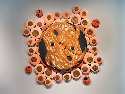 A collection of wooden circles surrounding a large disk with two fish carved into it
