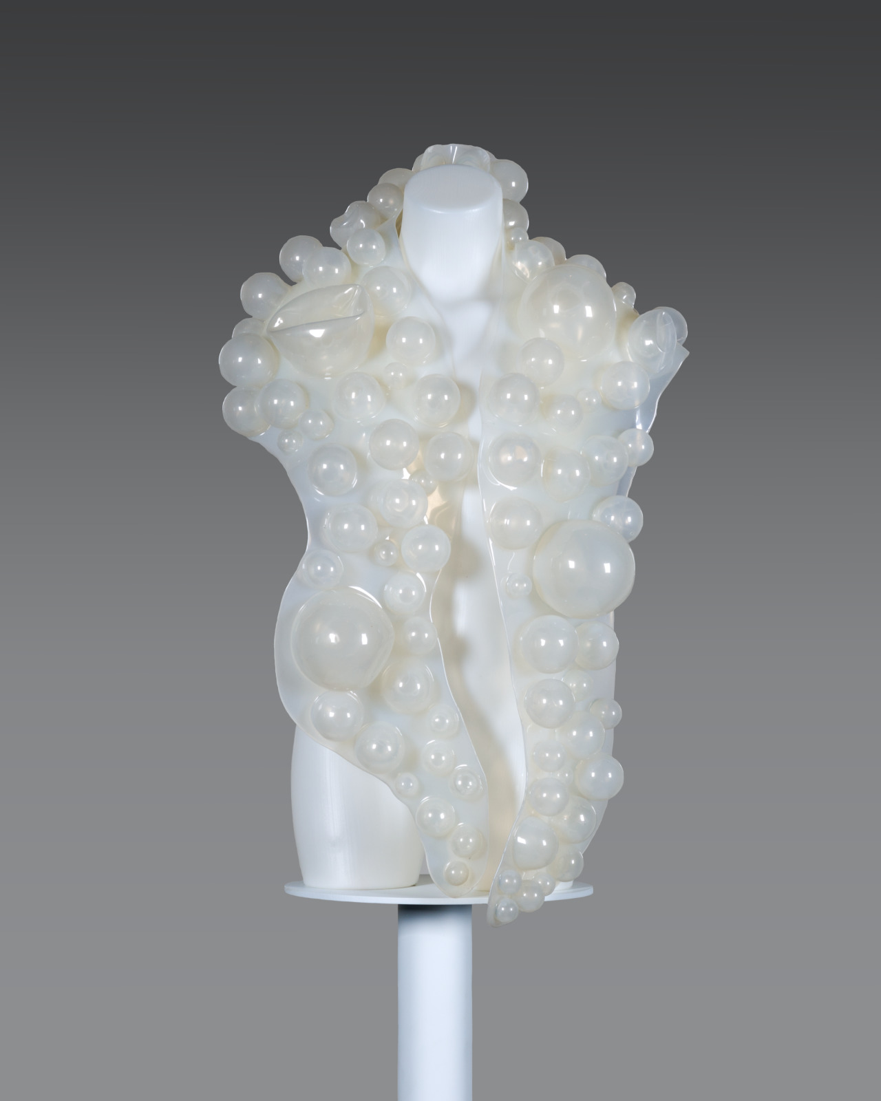 A mannequin torso draped in an opaque silicone shaw with opaque balls of varying sizes adhered to it