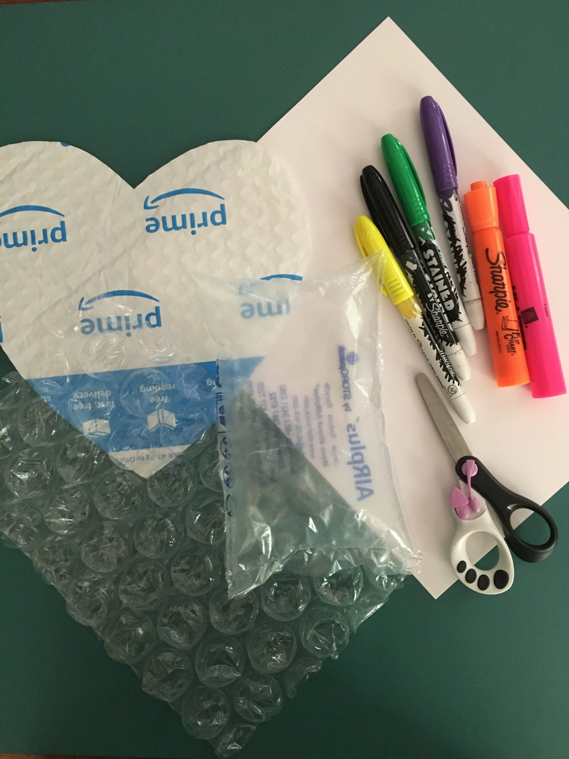 Supplies listed for this project grouped together on a table: bubble wrap, markers, scissors, paper, plastic bag