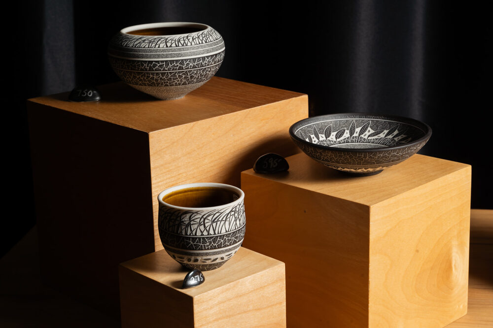 Three black and white pottery pieces arranged on wooden block.