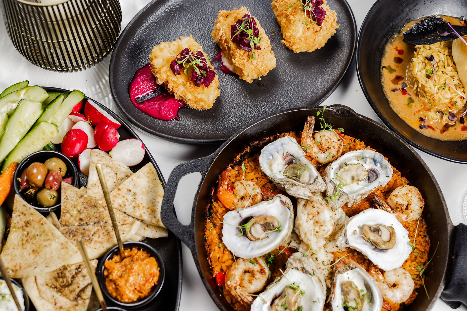 Four plates of food including oysters on the half-shell, pita and crudité, and two other dishes.