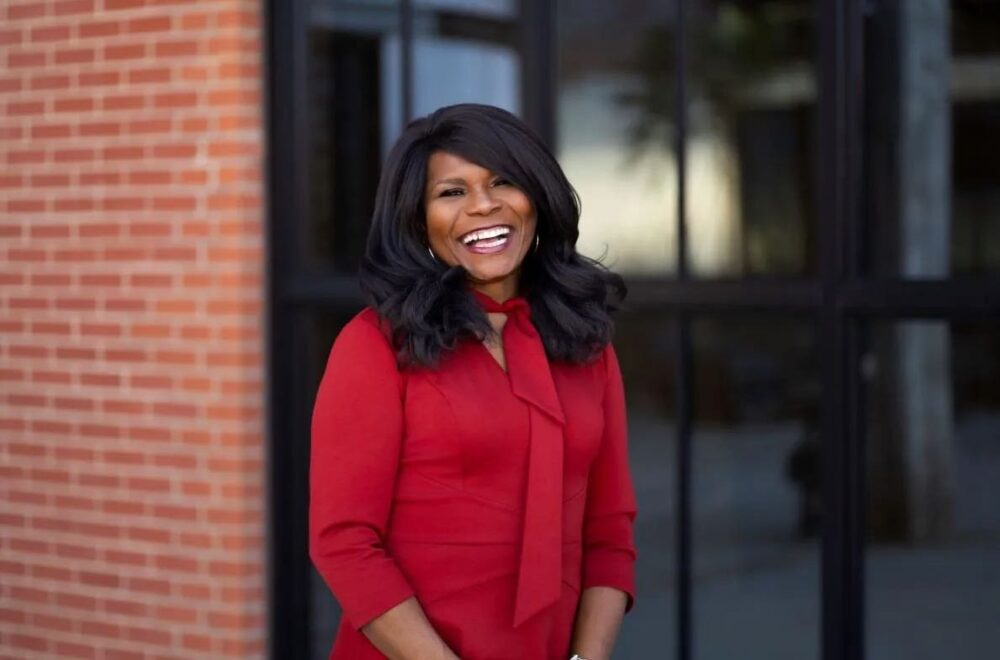 A Black woman with long hair standing in red dress in front of a brick building